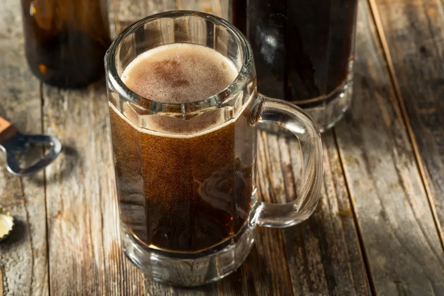 Dark homemade root beer in a glass mug on a rustic wooden table