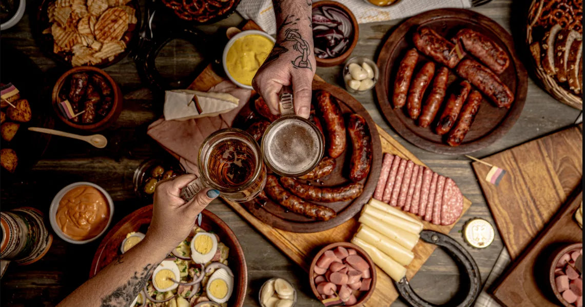 Oktoberfest food spread with sausages, pretzels, and two people toasting beers