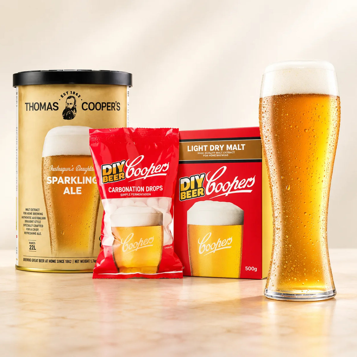 Coopers malt extracts ingredient set with Thomas Coopers extract can, carbonation drops, light dry malt, and a glass of golden beer.